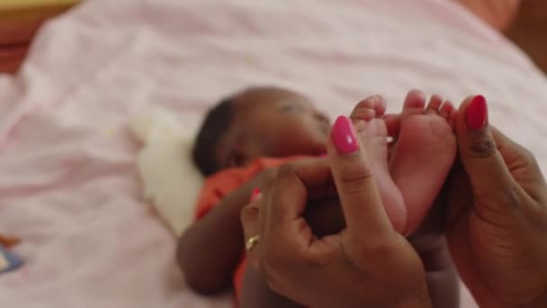 Cropped shot of mother holding feet of cute baby daughter lying on bed at home - Footage, Video