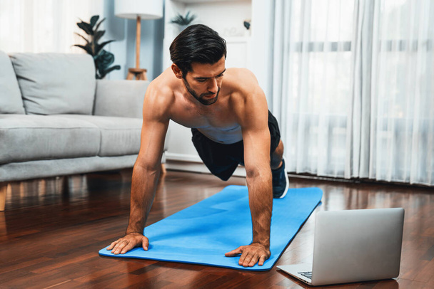 Atletyczny i sportowy mężczyzna robi pompki na macie fitness podczas sesji ćwiczeń online ciała dla sprawnego ciała i zdrowego stylu życia sportowego w domu. Gaiety domu ćwiczenia trening. - Zdjęcie, obraz