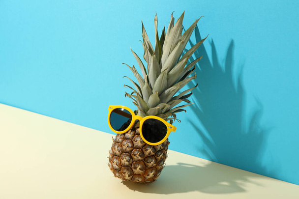 Piña con gafas de sol amarillas sobre fondo azul - Foto, Imagen