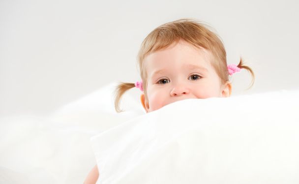 little girl peeping from of pillows in bed - Φωτογραφία, εικόνα