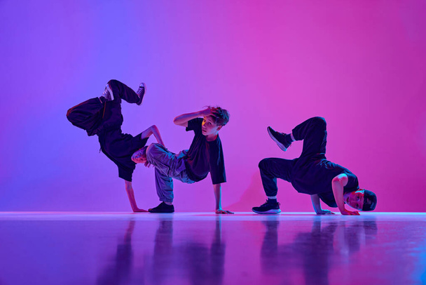 Tinédzserek csoportja, alkalmi öltözetben táncoló fiúk breakdance vegyes neo n light-ban vibráló gradiens háttér mellett. Koncepciója sport és hobbi, zene, divat és művészet, mozgás. Hirdetés - Fotó, kép