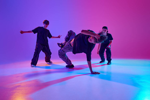 3人の若い男性ダンサーが活発な勾配の背景に対して混合されたネオンライトでストリートダンスバトルに参加します. スポーツ,趣味,音楽,ファッション,アート,ムーブメントのコンセプト。 アドベンチャー - 写真・画像
