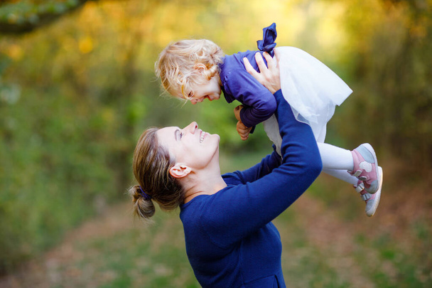 Happy young mother having fun cute toddler daughter, family portrait together. Woman with beautiful baby girl in nature and forest. Mum with little child outdoors, hugging. Love, bonding - Photo, Image