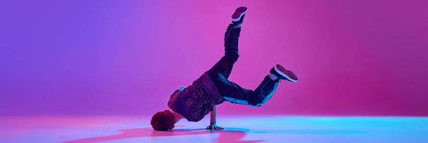 Sztandar. Nastolatek, break-tancerz wirujący na głowie w mieszanym świetle neonowym na żywym tle gradientowym. Odbiór. Pojęcie sportu i hobby, muzyki, mody i sztuki, ruchu. Ogłoszenie - Zdjęcie, obraz