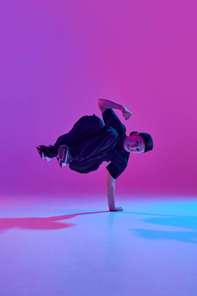 Een energieke dans. Jonge jongen die een complexe dansbeweging uitvoert in gemengd neon licht tegen levendige gradiënt achtergrond. Concept van sport en hobby, muziek, mode en kunst, beweging. Steun - Foto, afbeelding