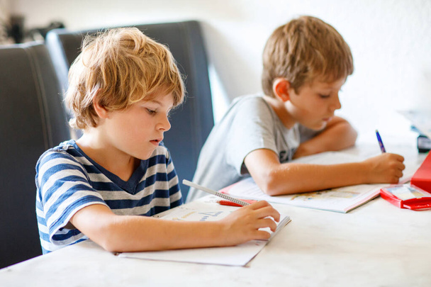 Zwei Jungen machen gemeinsam Hausaufgaben. Brüder, Geschwister und Zwillinge lernen zu Hause. Grundschüler, Kinder beim Schreiben - Foto, Bild