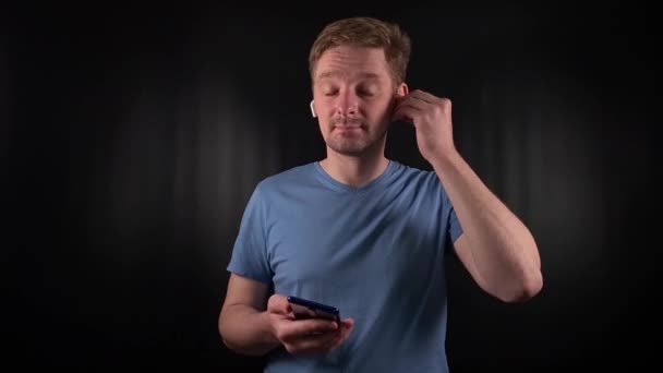 a stylish young man intently engages with a mobile device on a minimal black backdrop. His focused expression complements the sophisticated yet laid-back vibe. Modern lifes seamless tech integration - Footage, Video