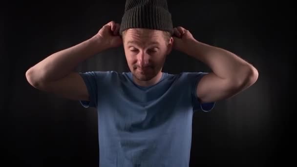A stylish young man puts on outfit, wearing a blue t-shirt with casual stubble with an air of casual look, his piercing gaze exuding an edgy yet confident attitude against the minimal black backdrop - Footage, Video