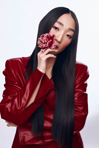 Elegante donna con lunghi capelli neri in giacca di pelle rossa con ritratto di fiori rosa - Foto, immagini