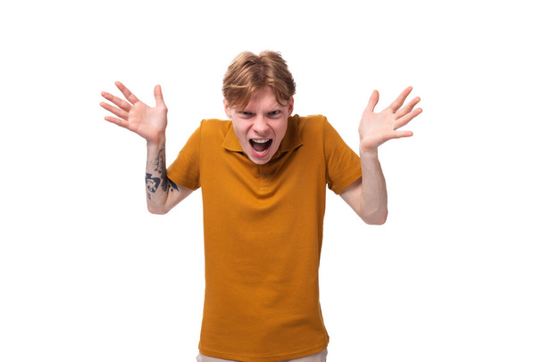 ein junger frustrierter Typ mit kurzen roten Haaren in einem sommerorangen T-Shirt schreit mit erhobenen Händen. - Foto, Bild