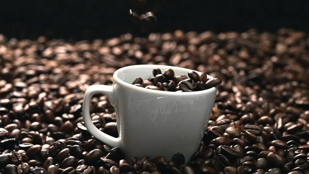 Sluiten van koffieboon vallen in een koffiekop omgeven door stapel bonen. aromatische bonen in een witte beker doen vallen. Bovenaanzicht van koffie druppel in glas met zwarte achtergrond. Bestanddelen. - Foto, afbeelding