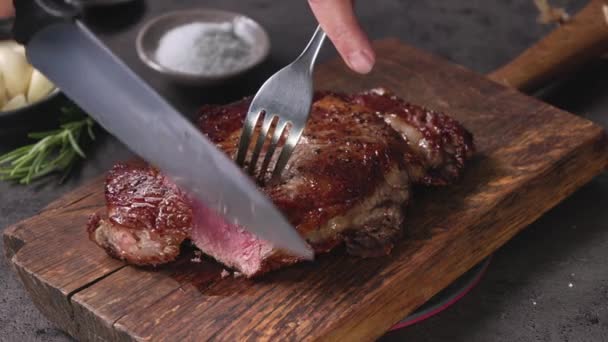 Σεφ τεμαχίζοντας φρεσκοψημένο ζουμερό κρέας μπριζόλας με μαχαίρι σε ξύλινη επιφάνεια κοπής στην κουζίνα, φαγητό σε κοντινό πλάνο - Πλάνα, βίντεο