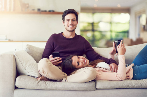 Tableta, teléfono y retrato de pareja en el sofá en la sala de estar para el entretenimiento juntos relajarse en casa. Feliz, el amor y la gente en red en el teléfono celular y la tecnología digital en el salón en el apartamento - Foto, Imagen