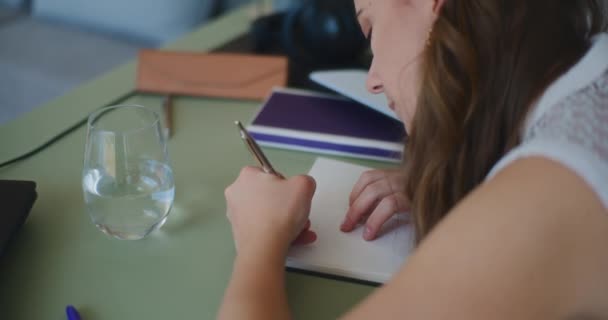 Mujer dedicada al aprendizaje en línea, anotando notas en su cuaderno - Metraje, vídeo