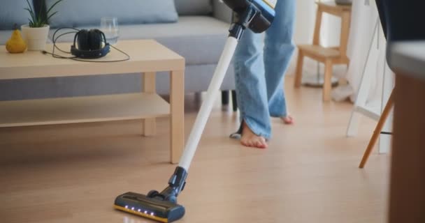 Pozytywna i uśmiechnięta kobieta szczęśliwie sprząta dom i usuwa kurz podczas odkurzania podłogi - Materiał filmowy, wideo