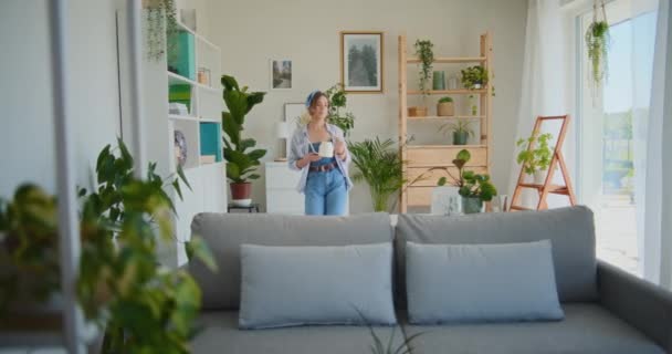 Une femme positive et joyeuse arrose joyeusement les fleurs à la maison, s'occupant de son jardin avec soin - Séquence, vidéo