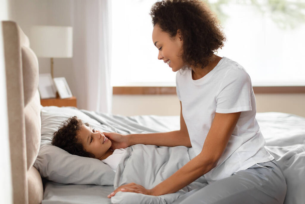 La madre afroamericana toca suavemente la cara de su hijo mientras comparten un momento amoroso en una mañana serena. Confort y afecto resuenan en este apacible comienzo del día. - Foto, imagen