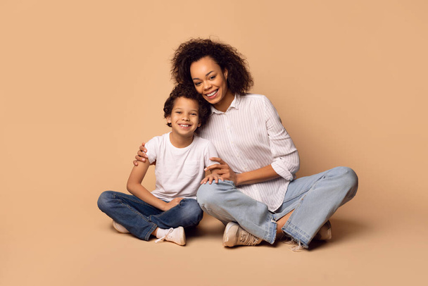 African American woman and a child are sitting on the ground, side by side. They appear to be engaged in a conversation or enjoying a moment of rest together - Photo, Image