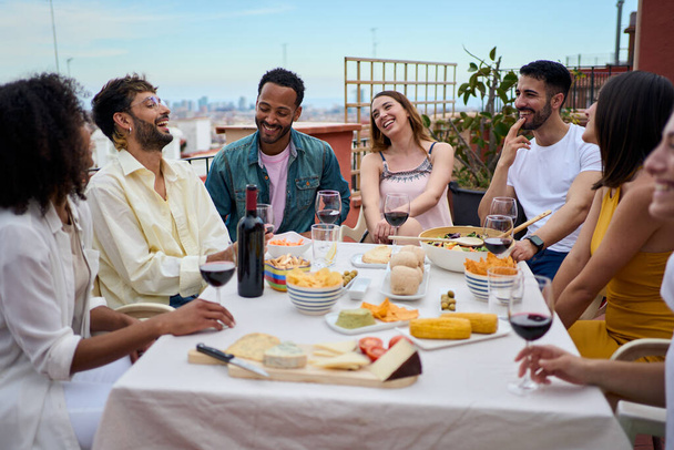 Grupo de jóvenes riéndose disfrutando del almuerzo juntos al aire libre. Reunión de amigos alegres celebrando la fiesta de comida en la terraza. Concepto de amistad milenaria y diversión en fin de semana - Foto, imagen