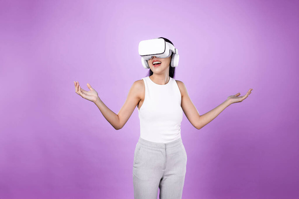 Mujer inteligente de pie con fondo rosa con auriculares VR que conectan tecnología de comunidad ciberespacial metaversa y futurista. Mujer elegante emocionado de ver generado paisaje virtual. Alucinaciones. - Foto, Imagen