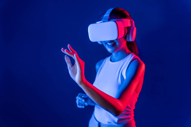 Okos nő áll körülvéve cyberpunk neon fény visel VR headset összekötő metaverse, futurisztikus cyberspace közösségi technológia. Egy nő kézfogással virtuális tárgyat használ. Hallucináció. - Fotó, kép