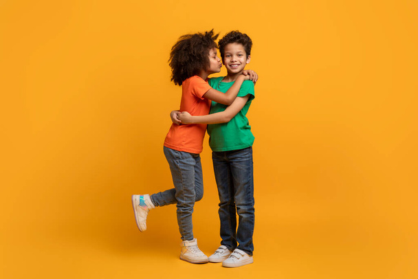 Dos niños afroamericanos se abrazan calurosamente sobre un fondo amarillo brillante. Sus rostros muestran alegría y afecto mientras comparten un abrazo sincero. - Foto, Imagen