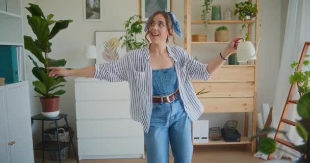 A smiling and positive girl dances joyfully with a watering can, enjoying life while watering flowers - Footage, Video