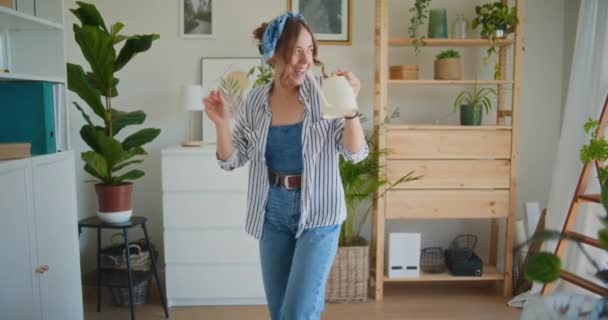 Ένα χαμογελαστό και θετικό κορίτσι χορεύει χαρούμενα με ένα ποτιστήρι, απολαμβάνοντας τη ζωή ενώ ποτίζει λουλούδια - Πλάνα, βίντεο