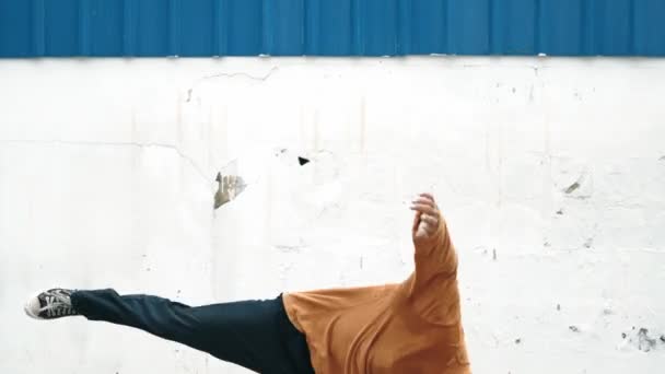 De Spaanse man strekt zijn armen uit en voert breakdances uit voor de muur. Closeup van stijlvolle street dancer in casual outfit oefenen dansen in hip hop stijl. Outdoor sport 2024. Achtergrond. hiphop. - Video