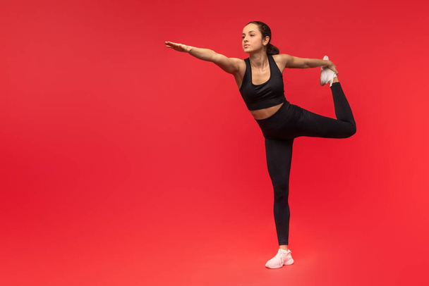 Uma mulher vestida com um top preto e leggings está demonstrando uma pose de ioga. Ela é focada e equilibrada, mantendo uma posição estável com precisão e controle - Foto, Imagem