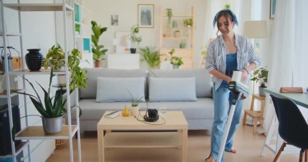 A positive and joyful woman cleans the room with a vacuum cleaner, radiating happiness - Footage, Video