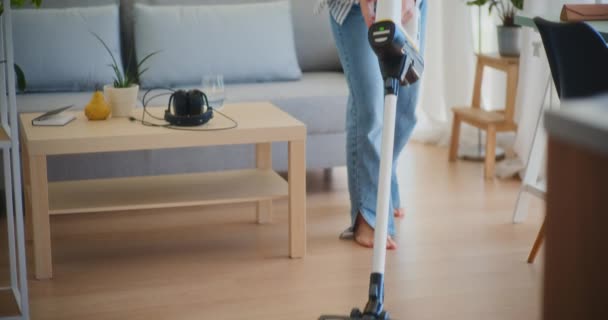 Positiivinen ja hymyilevä nainen puhdistaa iloisesti talon ja poistaa pölyn imuroidessaan lattiaa - Materiaali, video