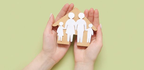Женские руки с фигурой семьи и деревянный дом на зеленом фоне - Фото, изображение