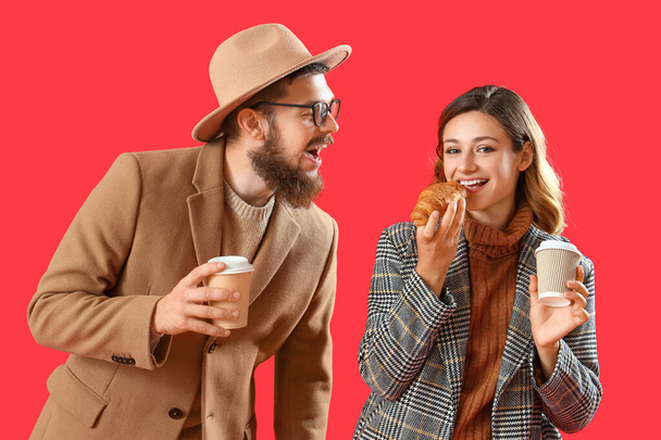 Happy couple in love with cups of coffee and croissant on red background - Photo, Image