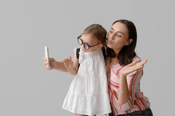 Belle mère et sa jolie petite fille avec téléphone portable prenant selfie sur fond gris - Photo, image