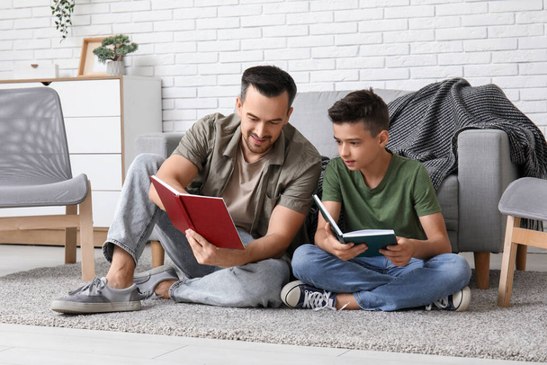Ο πατέρας και ο γιος του διαβάζουν βιβλία στο πάτωμα στο σπίτι. - Φωτογραφία, εικόνα