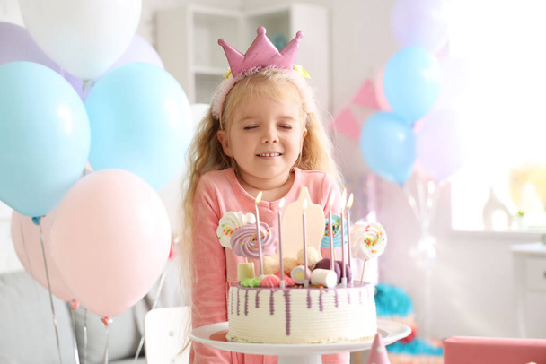 Schattig klein meisje in kroon met taart vieren verjaardag thuis - Foto, afbeelding