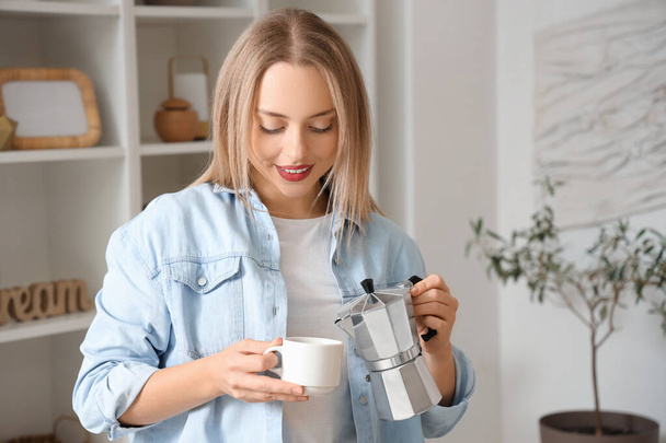 Csinos fiatal nő, aki kávét tölt a gejzír kávéfőzőből a csészébe a nappaliban. - Fotó, kép