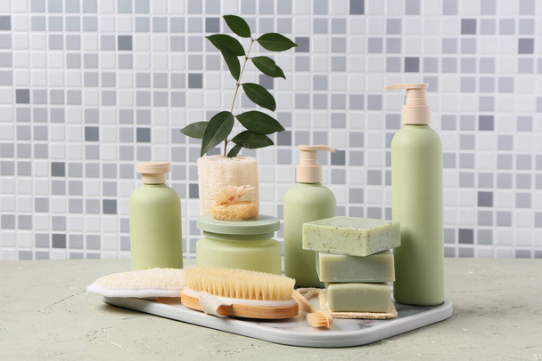 Plateau avec différents produits cosmétiques et fournitures de bain sur la table contre le mur de tuiles grises - Photo, image