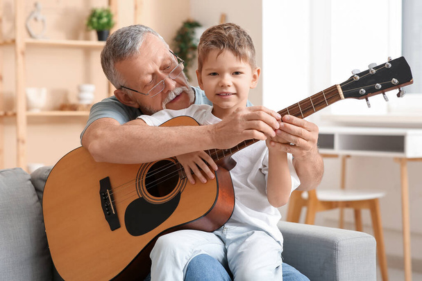 Ο παππούς διδάσκει τον εγγονό του παίζοντας κιθάρα στο σπίτι. - Φωτογραφία, εικόνα
