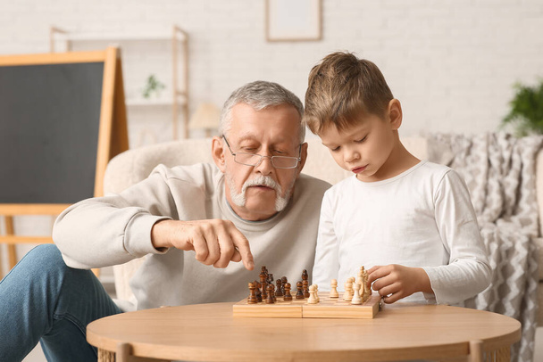 Büyükbaba ve küçük tatlı torunu evde satranç oynuyorlar. - Fotoğraf, Görsel