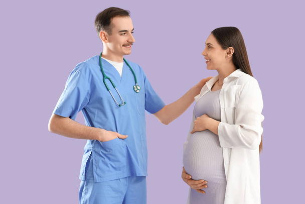 Mujer embarazada joven con médico sobre fondo lila - Foto, imagen