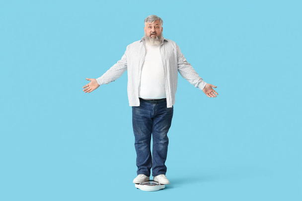 Overgewicht volwassen geschokte man met schubben op blauwe achtergrond. Gewichtsverlies concept - Foto, afbeelding