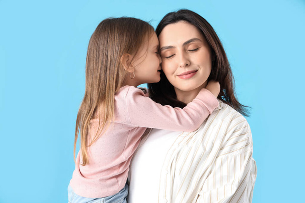 Giovane donna con la sua figlioletta carina che abbraccia su sfondo blu, primo piano. Festa della mamma celebrazione - Foto, immagini