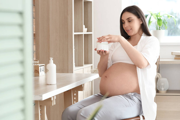 Молодая беременная женщина открывает банку сливок в домашнем офисе - Фото, изображение