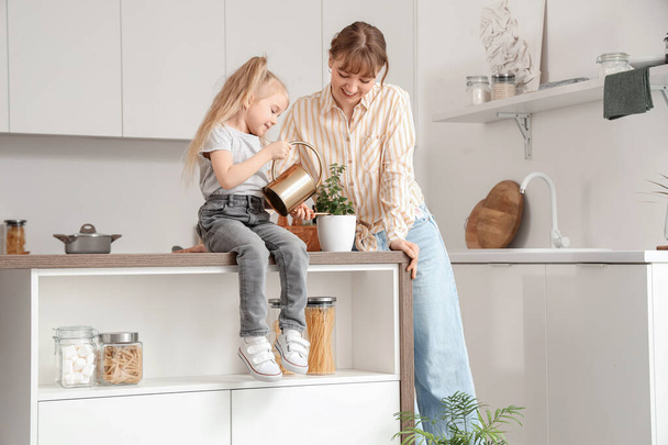 Nanny with little girl watering plant on table in kitchen - Photo, Image