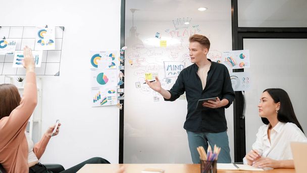 Professional male leader presents start up project by using mind map, colorful sticky notes and business statistic graph with confident while investor raising hand and asking question. Immaculate. - Photo, Image