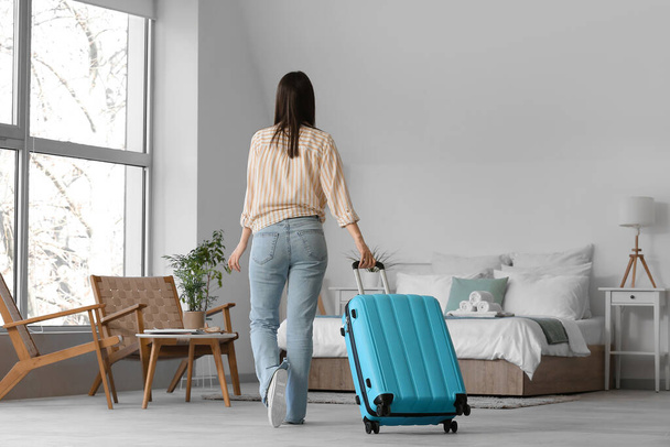 Bőröndös nő világos szállodai szobában, visszapillantás - Fotó, kép