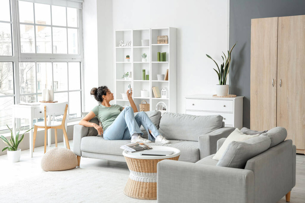 Young African-American woman turning on air conditioner in living room - Photo, Image
