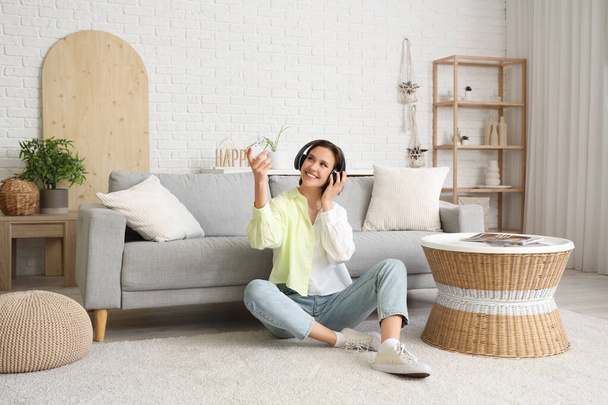 Mujer joven sonriente en auriculares con aire acondicionado control remoto sentado cerca del sofá en la sala de estar - Foto, imagen